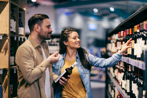Couple choosing which wine to buy before the 10pm closing time in the alcohol aisle at a supermarket in Scotland
