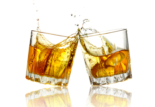 Two whisky glasses clink together as they toast a late night drink